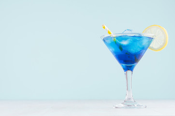 Exquisite blue cocktail for celebration in beach style with blue curacao, ice cube, lemon slice, yellow straw in mint color bar interior on white wood table.