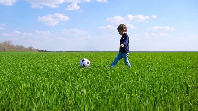Happy child running across a field of green grass and kicking a soccer ball in slow motion