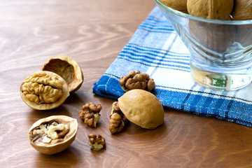 Whole walnuts and walnut kernel halves without shell on a dark wooden table and checkered towel, close up. Seeds of the common walnut tree Juglans regia. Macro food photo close up view.