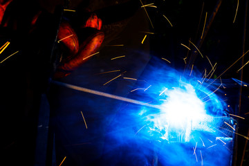 Welder worker performs jump welding. Man welder in protective gloves performs arc-welding process of metal structures. Flying sparks from the welding machine. Background construction site