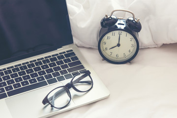 The laptop and alarm clock in the morning on a white bed. copy space. Lifestyle Concept