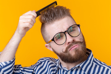 Portrait of a funny handsome young male hipster with a mustache and beard combing his hair against a yellow background. Barbershop concept and self-care.