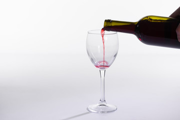 Red wine pouring into glass from bottle on white background with copy space