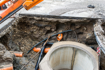 Building concrete sewage tank, flowing water trough orange pipes , excavator in the city.