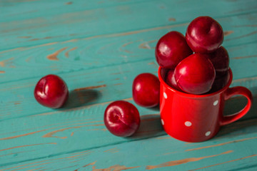 Fresh plums in a red mug on a wooden background.