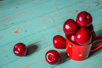 Fresh plums in a red mug on a wooden background.