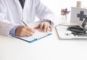 Fototapeta premium Close up male doctor or medical student using mobile smart phone working on laptop computer in hospital with copy space.