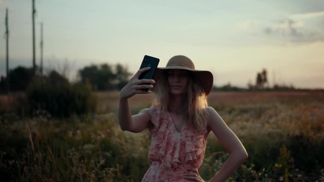 Woman In Hat Takes Selfie At Sunrise.Selfie At Sunrise.Blonde Woman Taking Selfie At Sunset In Field.Girl Taking Photo And Smailing.Woman Portrait At Sunset.Beautiful Woman Enjoing Nature At Sunset.