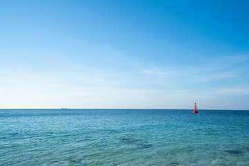 Obraz premium Landscape wide shot selective focus the blue ocean sea at tropical island in summer day. Red buoy floating in sea with sky and clouds backgrounds. The sun glimmering sunlight peeking the sea surface