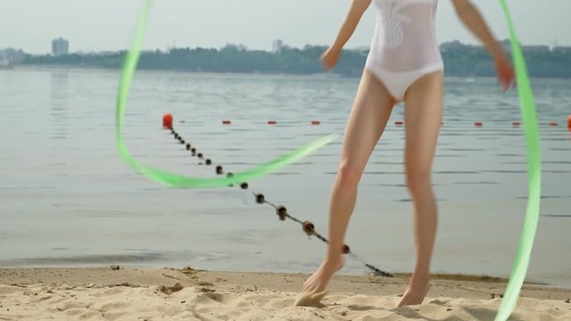 young woman gymnast in a white body on a sandy beach dancing with gymnastic ribbon. Summer, dawn