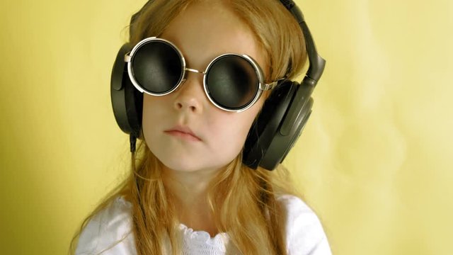 Cheerful little girl in headphones on a yellow background. Closeup portrait.