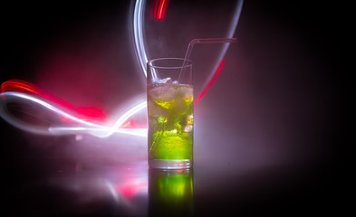 Cocktail glass splashing on dark toned smoky background or colorful cocktail in glass. Party club entertainment. Mixed light.