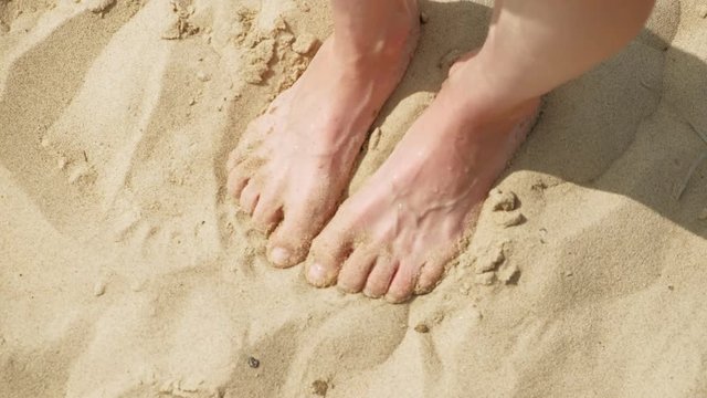 Feet are on the sand near the water. Beach. Summer sunny day