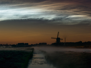 Windmill, fog banks and bright noctilucent clouds (NLC) over the dutch landscape during a midsummer night