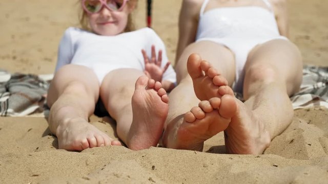 Mom and daughter are sunbathing on the beach. Summer sunny day
