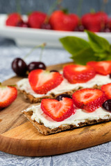 bread with cottage cheese, fresh strawberries and cherries on a wooden Board, on a gray background, selective focus