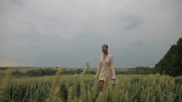 An African American girl goes through a green field. Colored girl happy. Beautiful nature, the model is dressed in lightweight dress.