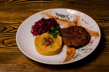 closeup two pieces of medium raw grilled meat decorated with red pepper and sauce served with potato chips and vegetable salad on black restaurant plate on wooden table.