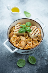 Orecchiette with grilled cheese, sun dried tomato pesto and green basil in a pan, studio shot on a grey stone background