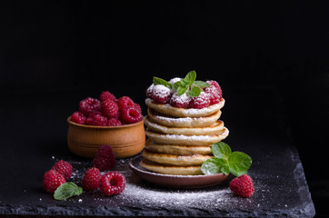Pancakes with raspberries and berries around on black backgound