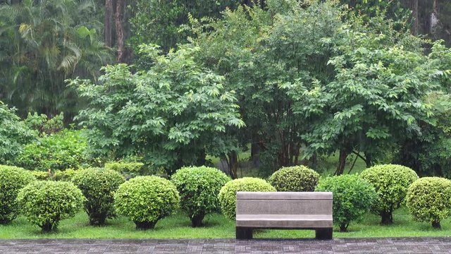 Heavy rain is falling on the pavement and modern wooden bench outdoors in the park. front view