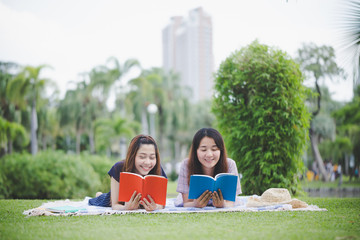 Education outdoor, Young beautiful smiling woman read books lying on a fabric of the city park.