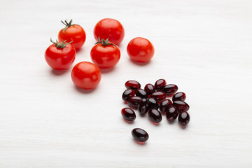 Beautiful red tomatoes lie next to the red jelly vitamins on the white table. Concept of trace elements and vitamins in the summer and winter.