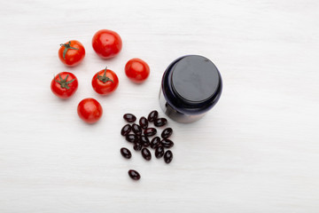 Tomatoes lie on a white table next to vitamins in the form of jelly next to a jar on a white table. Concept of vitamins and minerals.