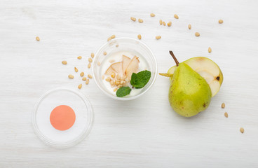 Yogurt pear slices and mint and pine nuts lie in a lunch box on a white table next to scattered with pine nuts and pear slices. Healthy eating concept.