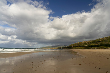 Deep Atlantic Ocean water colors, breaking waves in a sandy beach, spectacular clouds in the sky. Romantic Spring Morning at Bologna Beach, Tarifa, Cadiz, Andalusia, Spain, Europa.