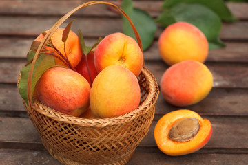 Naklejka na ściany i meble Apricot. Ripe Organic Apricots in wicker basket with fresh leaves on a wooden table.