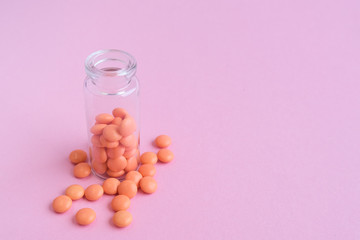 Orange tablets from glass bottle on pink background. copyspace for text. Epidemic, painkillers, healthcare, treatment pills and drug abuse concept