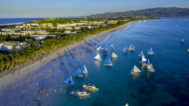 Aerial Hyperlapse of sail boats and people on a large, busy beach watching sunset (White Beach, Boracay, Philippines)