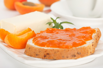 Apricot jam in a glass jar and fresh apricots on a table. Bread slice with butter and apricot marmalade for breakfast.