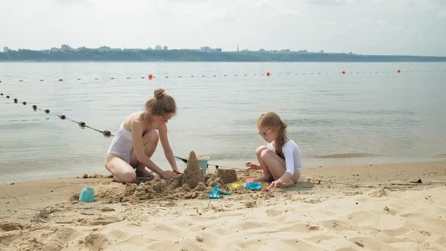 Mom and daughter are playing on the beach, building a sand castle. Summer sunny day. vacation