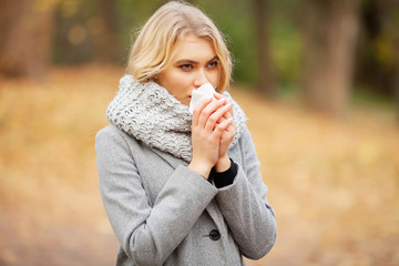 Girl sneezing in tissue. Young woman blowing her nose on the park. Woman portrait outdoor sneezing...