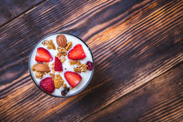 Obraz na płótnie Canvas Health concept - Top view bowl of homemade granola with yogurt and fresh strawberries on wooden background.