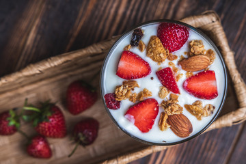 Health concept - Top view bowl of homemade granola with yogurt and fresh strawberries on wooden background.