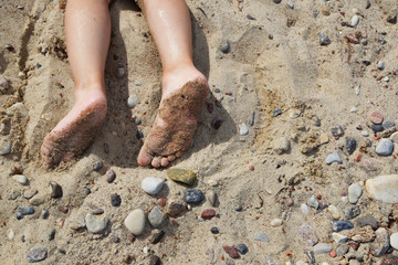 Two wet sandy bare feet of child  boy in sand with pebbles at  beach relaxing in summer day.