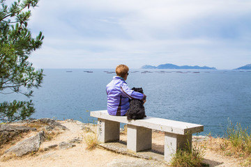 woman sitting with her dog on the bench relaxed admiring the Cies islands in the sea