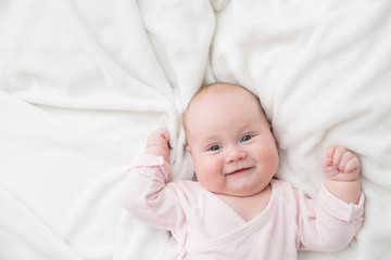 Newborn baby girl posed on her back, on blanket of fur, smiling looking at camera