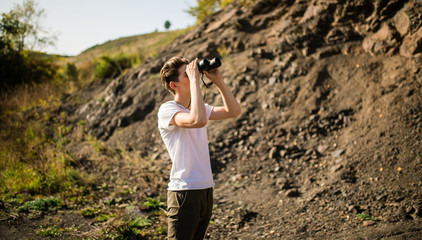 Young man holding a binoculars looking on top of mountain