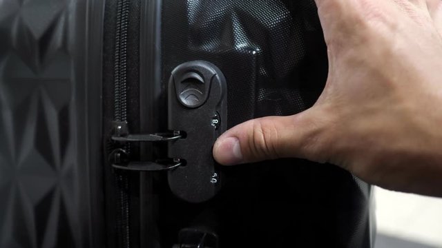 Man is testing lock. He enters the code to open suitcase combination lock on the suitcase and presses the button, hands closeup.