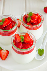 Dietary creamy yogurt panna cotta with fresh strawberry sauce in glass jars.