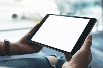 Mockup image of a woman's hands holding and using black tablet pc with blank white screen while sitting in the airport