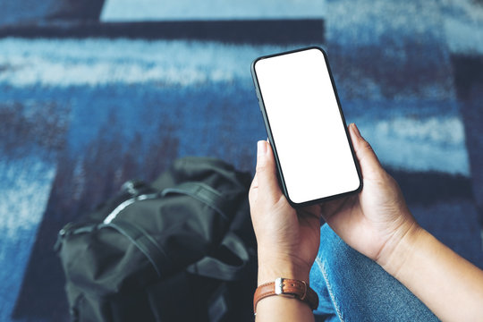 Mockup image of a woman's hands holding and using black mobile phone with blank screen while sitting in the airport
