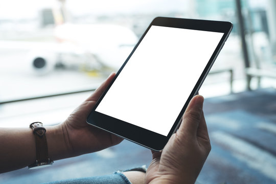 Mockup image of a woman's hands holding and using black tablet pc with blank white screen while sitting in the airport