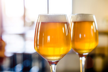 Two glasses of beer are on the bar table. 