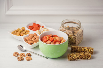 Granola cereal flakes with dried fruit, nuts in green bowl on white wooden table.