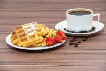 Viennese waffles sprinkled with powdered sugar, with strawberries and a cup of coffee.